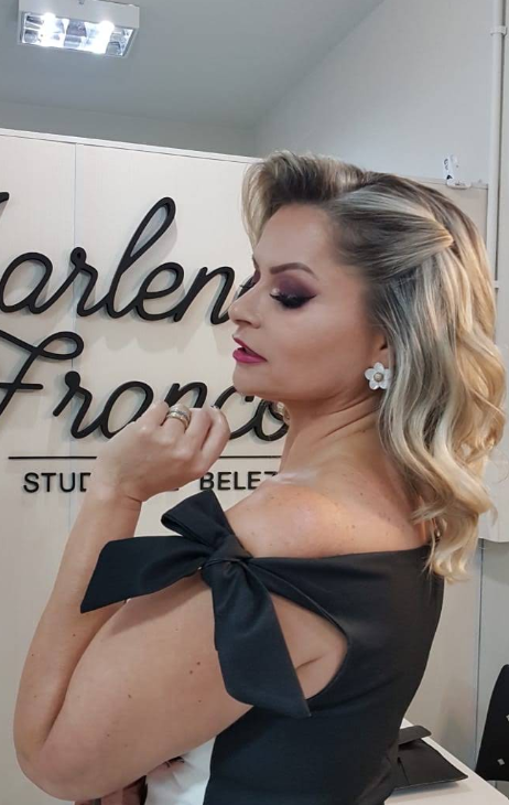 Cliente com penteado e maquiagem prontos ao lado do letreiro do Marlene Franco Studio de Beleza